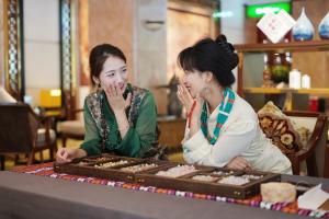 twee vrouwen die aan een tafel zitten en naar koekjes kijken bij Chengdu Tibetan Hotel-Free Welcome Tibetan Tea in Chengdu