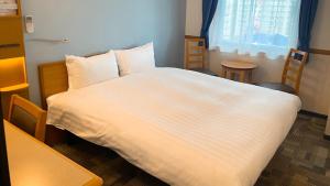 een slaapkamer met een wit bed met stoelen en een raam bij Toyoko Inn Mito-eki Minami-guchi in Mito