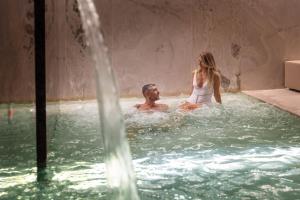 Un uomo e una donna seduti in una vasca idromassaggio di LLAC Living Nature Hotel a Limone sul Garda