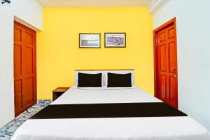 1 dormitorio con cama y pared amarilla en Super Hotel O Vijaynagar Road formerly Anmol Peace Stay, en Ooty