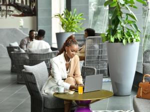 una donna seduta a un tavolo con un portatile di Novotel Nairobi Westlands a Nairobi