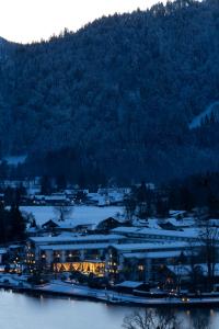 un grand bâtiment sur la rive d'une masse d'eau dans l'établissement Althoff Seehotel Überfahrt, à Rottach-Egern