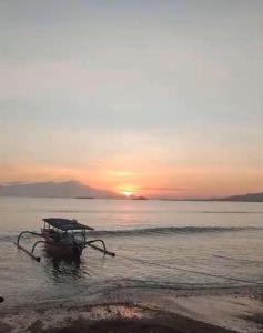 una barca sulla spiaggia con il tramonto sullo sfondo di Gili Gede Homestay a Gili Gede