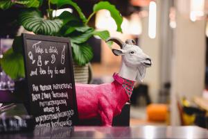 eine Figur einer rosa Ziege neben einem Schild in der Unterkunft Moxy Poznań Airport in Posen