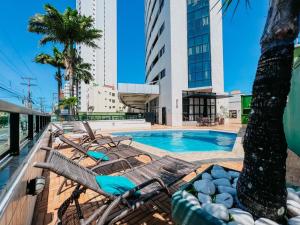 a swimming pool with lounge chairs and a palm tree at Natal Plaza Suítes- Ponta Negra in Natal