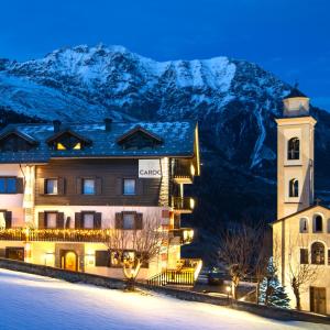 un bâtiment avec une tour d'horloge en face d'une montagne dans l'établissement Hotel Cardo, à Valdidentro