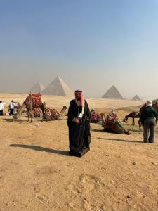 Un uomo in piedi nel deserto con delle piramidi sullo sfondo di New pyramids way a Il Cairo