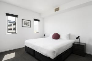 a white bedroom with a large bed and two windows at Tyrian Serviced Apartments Fitzroy in Melbourne