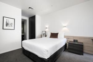 a bedroom with a large white bed and a table at Tyrian Serviced Apartments Fitzroy in Melbourne