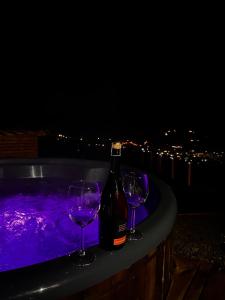 een fles wijn en twee wijnglazen naast een hot tub bij Under Sky Slavske - Котеджі з приватним чаном-джакузі, панорамною ванною та PlayStation 5 in Slavske