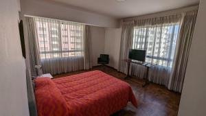 a bedroom with a red bed and two windows at Habitaciones Frente Club Tenis in Cochabamba