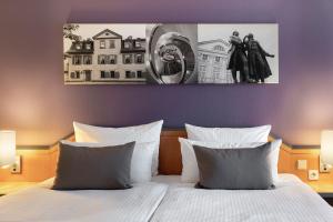 1 cama con almohadas blancas y una pintura en la pared en Leonardo Hotel Weimar, en Weimar