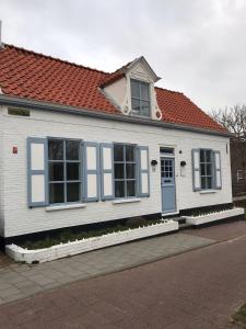 ein weißes Haus mit blauen Fenstern und einem roten Dach in der Unterkunft B&B Zee van Tijd Domburg in Domburg