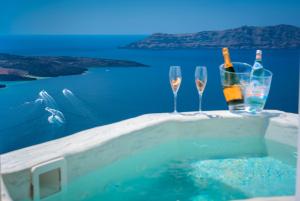 deux verres à vin et des bouteilles sur une table à côté de l'eau dans l'établissement Modernity Suites, à Fira