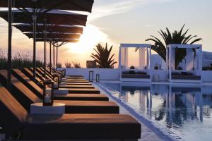 a resort pool with benches and an umbrella at Livin Mykonos Hotel - Adults Only in Mýkonos City