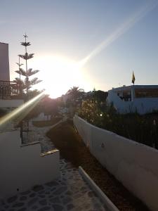 a sun setting behind a white wall with a tree at Archipelagos in Naxos Chora