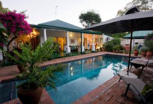 una piscina con sombrilla junto a una casa en York Lodge, en Harare