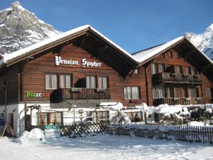 un grande edificio in legno con neve sul terreno di Hotel Pension Spycher a Kandersteg