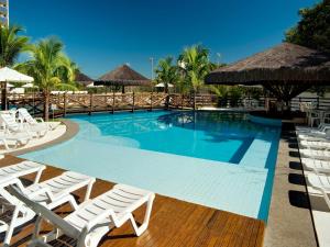 une grande piscine avec des chaises et des parasols blancs dans l'établissement Apartamento Suites Le Jardin Caldas Novas Goiás, à Caldas Novas