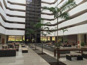 un hall avec des tables et des palmiers dans un bâtiment dans l'établissement Apartamento Suites Le Jardin Caldas Novas Goiás, à Caldas Novas