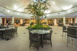 un vestíbulo con mesas, sillas y una palmera en Hotel Vip Grand Maputo en Maputo