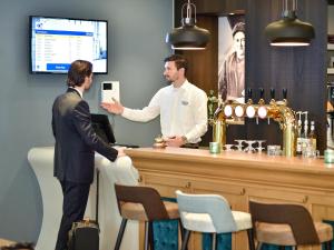 Zwei Männer stehen an einer Bar mit einem Mann, der eine Tafel hält. in der Unterkunft Brasserie-Hotel Antje van de Statie in Weert