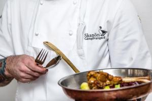 a chef holding a fork and a bowl of food at Skanörs Gästgifvaregård in Skanör med Falsterbo