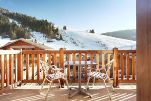 uma mesa e cadeiras num deque com uma montanha coberta de neve em Hôtel Prestige Odalys Le Chamois em La Clusaz