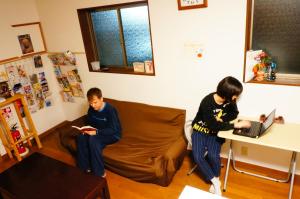 twee mensen zitten op een bank in een woonkamer bij Osaka Tomato Guesthouse in Osaka