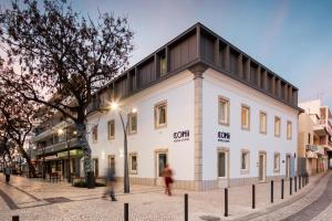 um edifício branco com um telhado preto numa rua em Hostel Conii & Suites Algarve em Quarteira