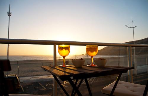 uma mesa com dois copos numa varanda com praia em Batata - Ocean View na Nazaré