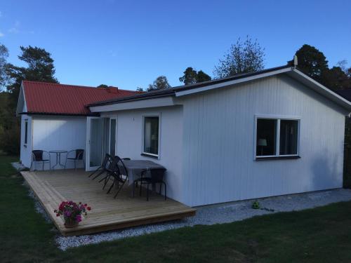 Cette petite maison blanche dispose d'une terrasse en bois. dans l'établissement Ringbomsvägen Holiday Home, à Ljugarn