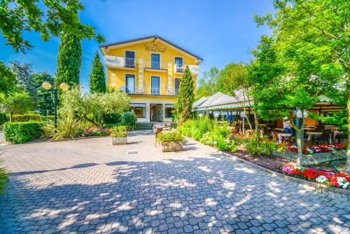 ein gelbes Gebäude mit Bäumen und Blumen im Innenhof in der Unterkunft Hotel Riel in Sirmione