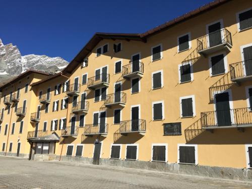 a yellow building with balconies and mountains in the background at Residence Redicervinia in Breuil-Cervinia