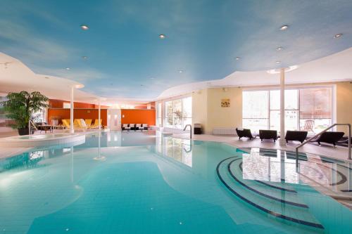 a large swimming pool in a hotel with chairs and tables at Landhaus Zu den Rothen Forellen in Ilsenburg