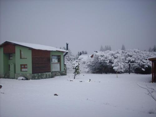 un patio cubierto de nieve con una casa y árboles en Cabañas Ruca Carel, en San Carlos de Bariloche