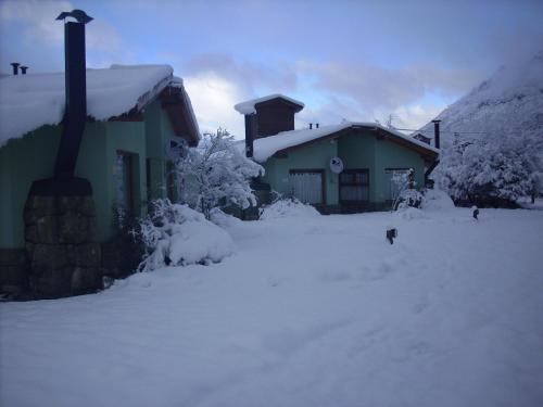 una casa cubierta de nieve con un perro delante de ella en Cabañas Ruca Carel, en San Carlos de Bariloche