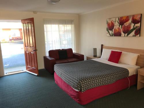 ein Schlafzimmer mit einem Bett, einem Stuhl und einem Fenster in der Unterkunft Beachcomber Motel & Apartments in Apollo Bay