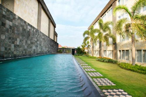 - une piscine à côté d'un bâtiment avec des palmiers dans l'établissement Aston Denpasar Hotel & Convention, à Denpasar