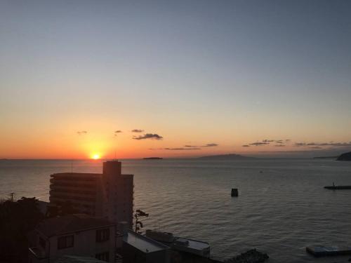 een zonsondergang boven het water met een gebouw op de voorgrond bij Atami Onsen Guest House Megumi in Atami