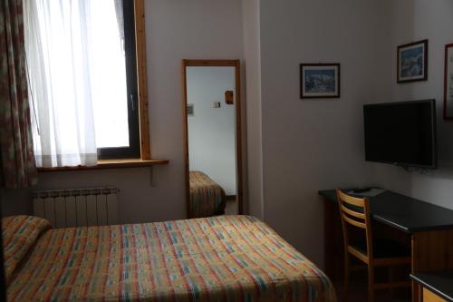 Cette chambre comprend un lit, un bureau et une télévision. dans l'établissement Hotel Dolomiti, à Passo del Tonale