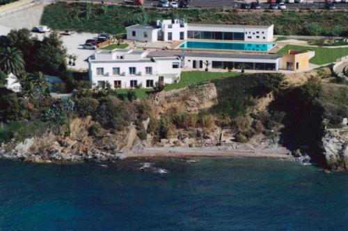 a large white house on a cliff next to the ocean at La Rosa dei Venti Resort in Piombino