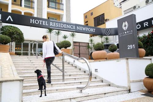 Eine Frau, die einen schwarzen Hund die Treppe hinaufgeht. in der Unterkunft Vitória Hotel Residence NewPort in Campinas