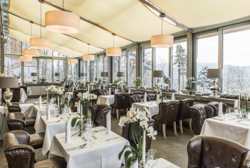 un restaurante con mesas y sillas blancas y ventanas en Berghotel Eisenach, en Eisenach