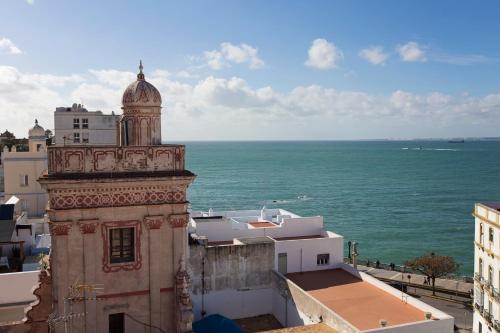 een gebouw met een klokkentoren naast de oceaan bij Hotel Casa de las Cuatro Torres in Cádiz