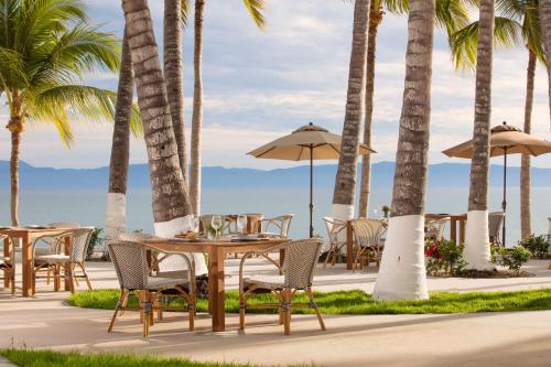 Vista Vallarta All Suites On The Beach في بوسيرياس: طاولة وكراسي على الشاطئ مع أشجار النخيل