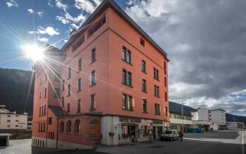 un edificio alto rojo con el sol brillando en él en Hotel Ochsen by Mountain Hotels, en Davos