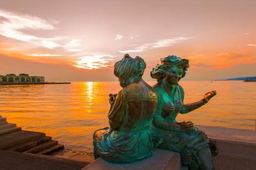 eine Statue von zwei Frauen, die bei Sonnenuntergang neben dem Wasser sitzen in der Unterkunft Residence Theresia- Tailor Made Stay in Triest