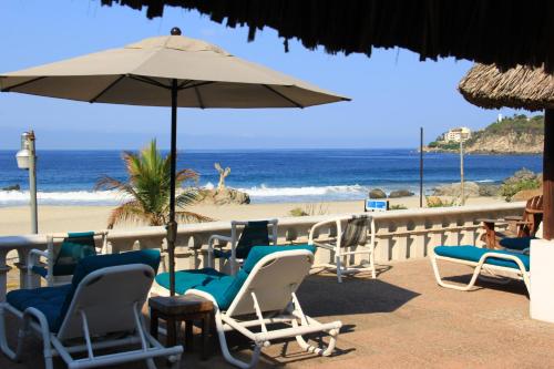 a beach with chairs and an umbrella and the ocean at Hotel Santa Fe in Puerto Escondido