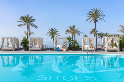 a swimming pool with chaise lounge chairs and palm trees at ME Sitges Terramar in Sitges